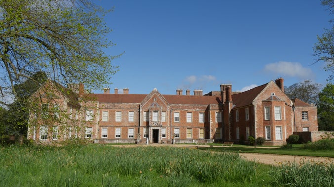 A historic house sits at the end of a long driveway surrounded by greenery.